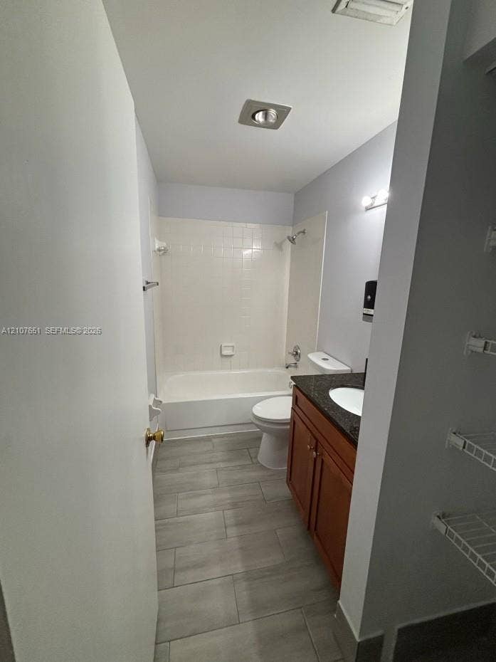 Bathroom featuring a vanity with a stone-finish countertop, under-mount sink, wood-finish cabinetry, tile flooring, and a tub-shower combination with tile surround