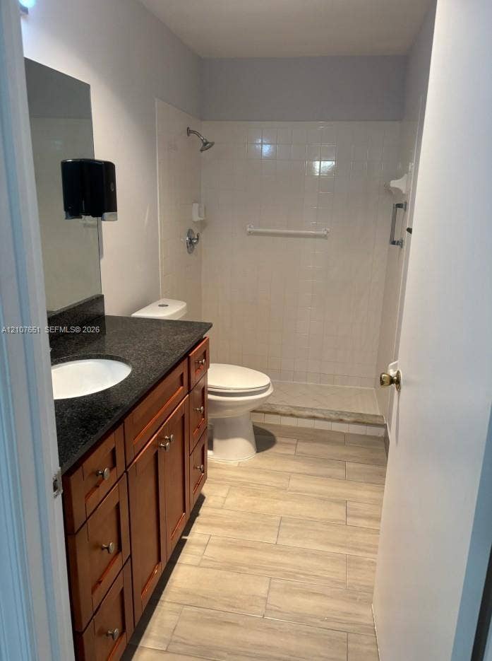 Bathroom featuring wood-finish cabinetry, dark countertop with an integrated basin, tile flooring, and a tiled shower stall