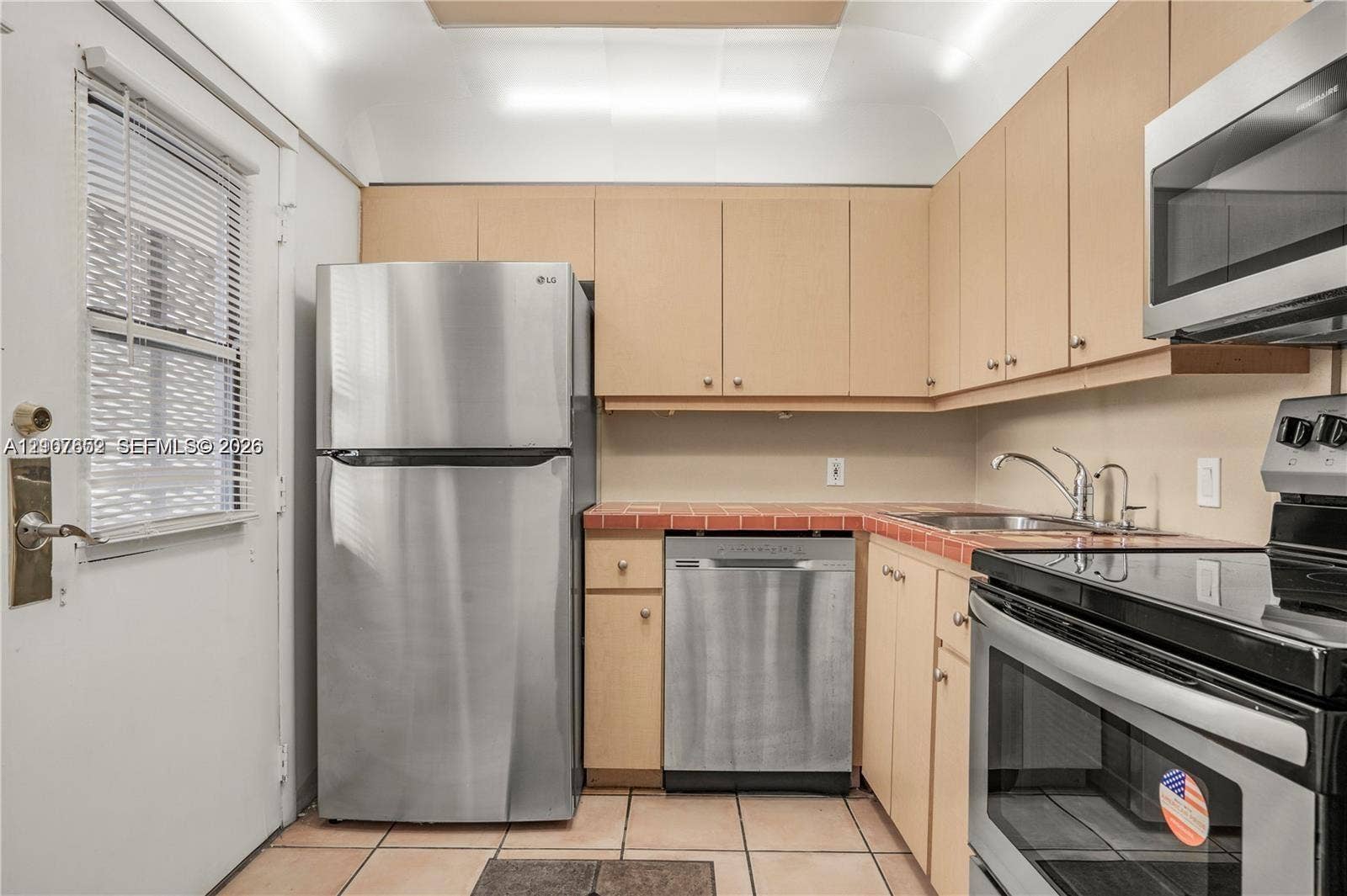 20500 W Country Club Drive, #607, Aventura, Aventura, FL 33180 Kitchen featuring flat-panel wood cabinetry, tile countertops, tile flooring, and a stainless steel appliance package including a refrigerator, dishwasher, and microwave