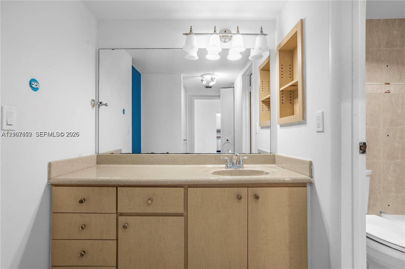 20500 W Country Club Drive, #607, Aventura, Aventura, FL 33180 Vanity featuring wood-finish cabinetry, solid-surface countertop, integrated sink, large wall-mounted mirror, and four-light overhead fixture