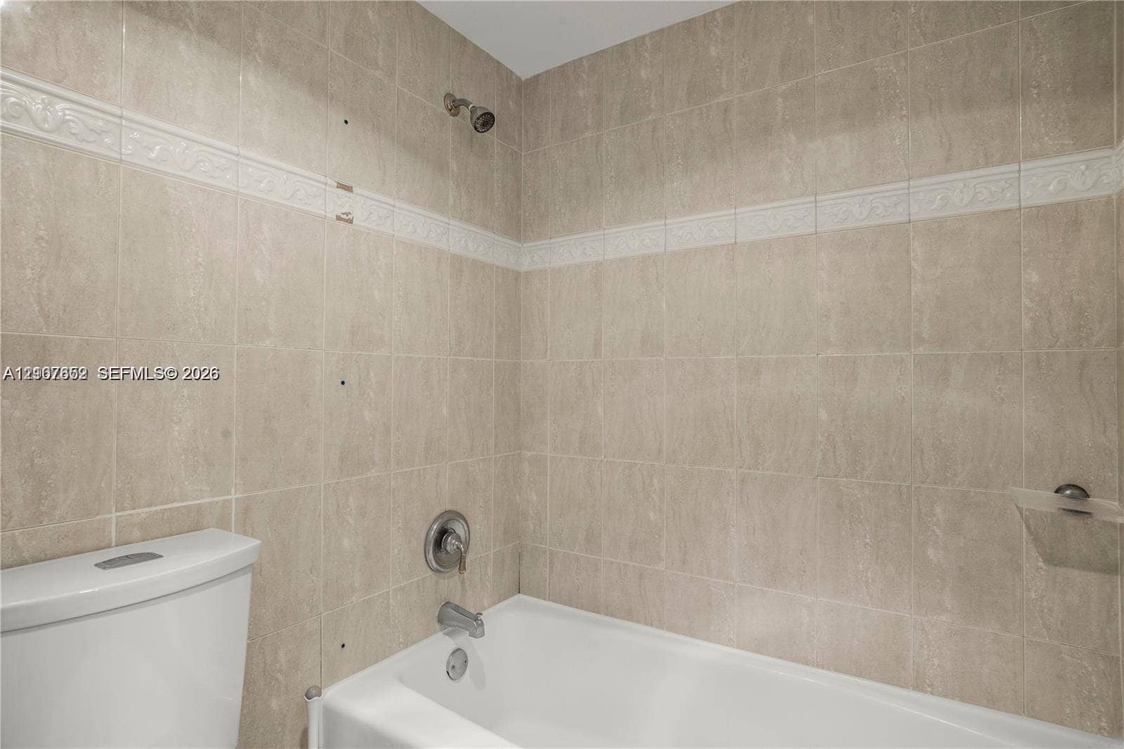 20500 W Country Club Drive, #607, Aventura, Aventura, FL 33180 Bathtub and shower combination featuring neutral-toned wall tiles with a decorative accent border, a built-in recessed soap dish, and chrome-finish plumbing fixtures