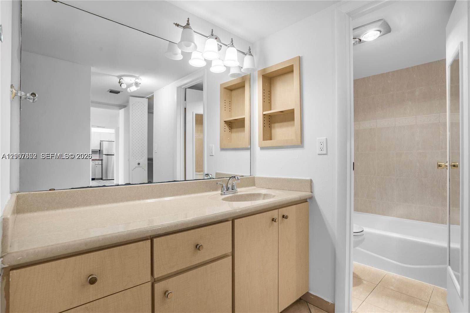 20500 W Country Club Drive, #607, Aventura, Aventura, FL 33180 Bathroom featuring a vanity with integrated countertop and sink, light wood-finish cabinetry, built-in wall shelving, a full-width mirror, and a tiled shower-tub enclosure