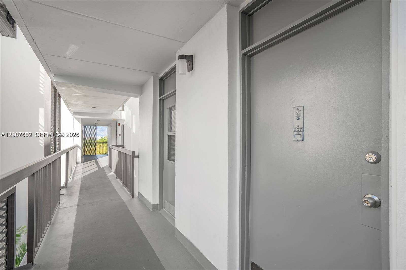 20500 W Country Club Drive, #607, Aventura, Aventura, FL 33180 Covered exterior walkway featuring a solid-panel door, wall-mounted light fixture, and metal railing