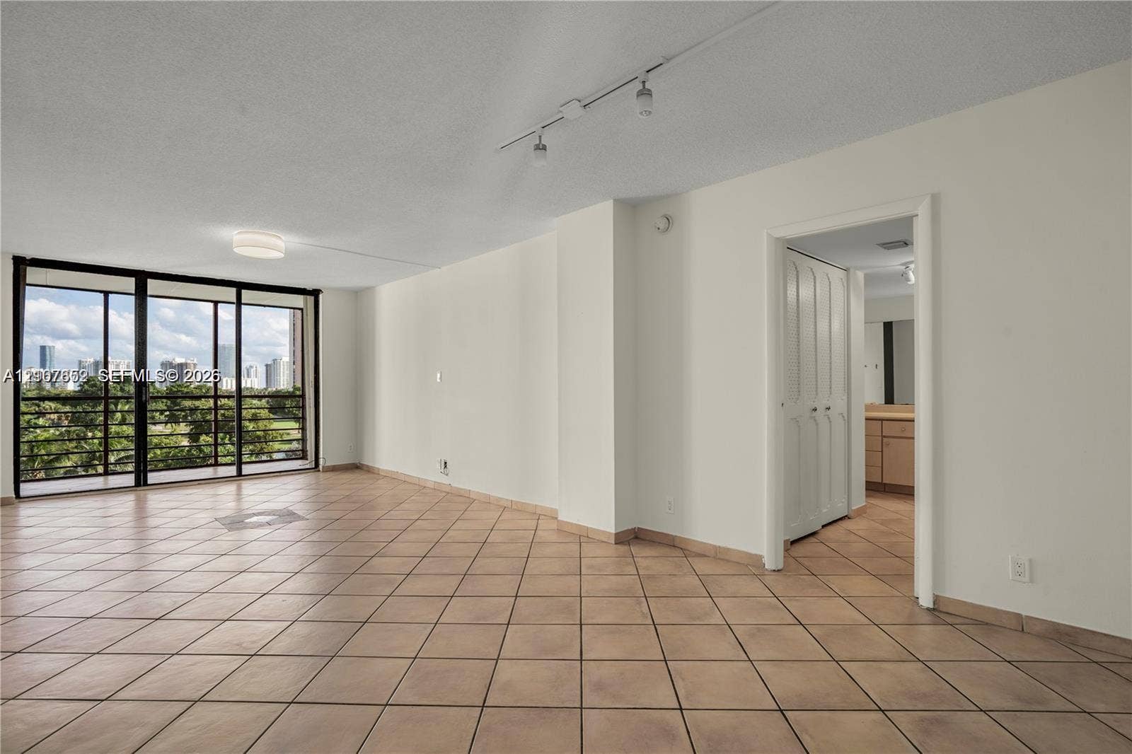 20500 W Country Club Drive, #607, Aventura, Aventura, FL 33180 Open living space featuring neutral tile flooring, floor-to-ceiling sliding glass doors, adjustable track lighting, and built-in closet storage