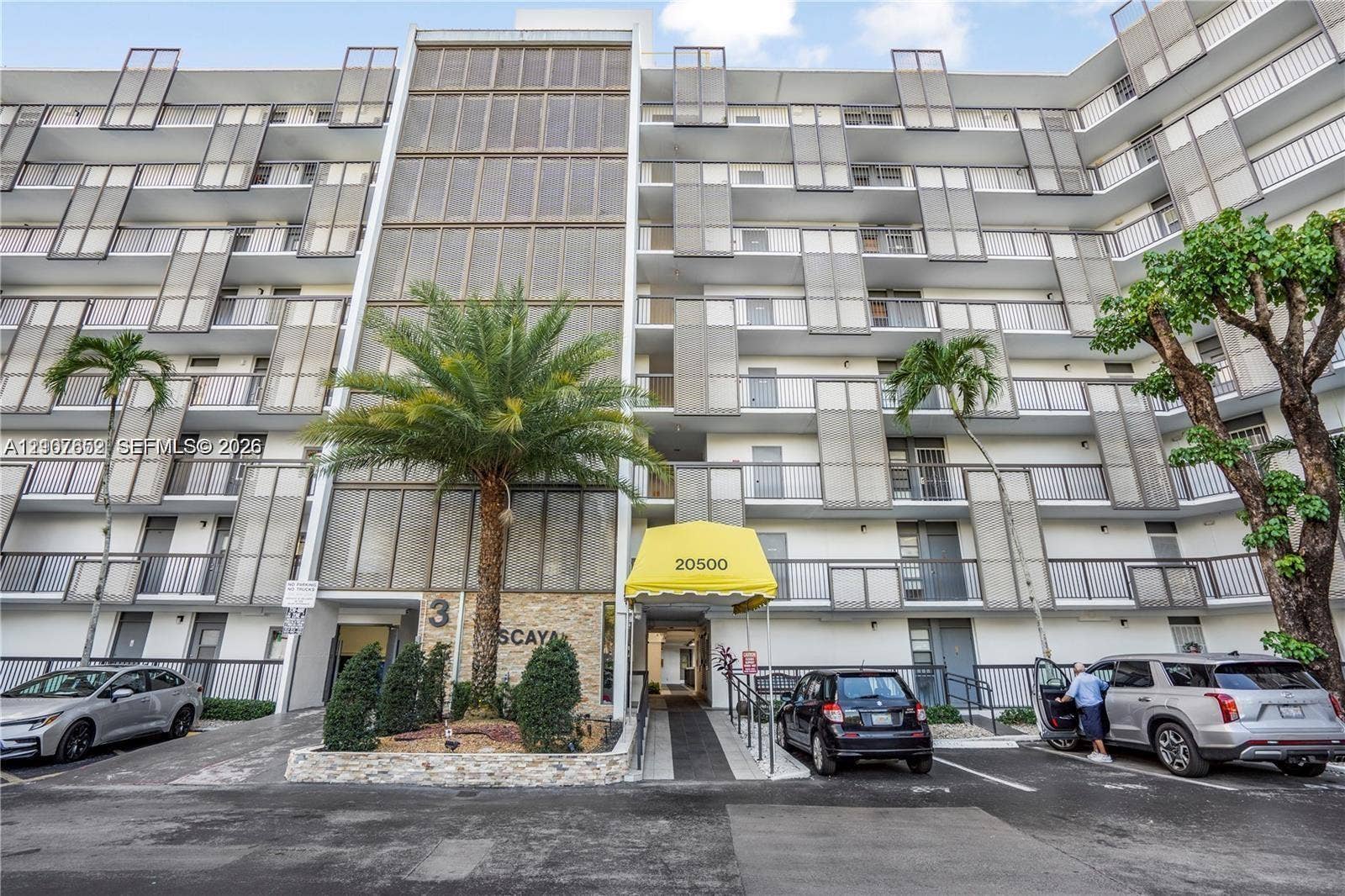 20500 W Country Club Drive, #607, Aventura, Aventura, FL 33180 Mid-rise building exterior featuring a stone-clad facade, private balconies with metal railings, decorative metal screening, and an integrated covered entrance