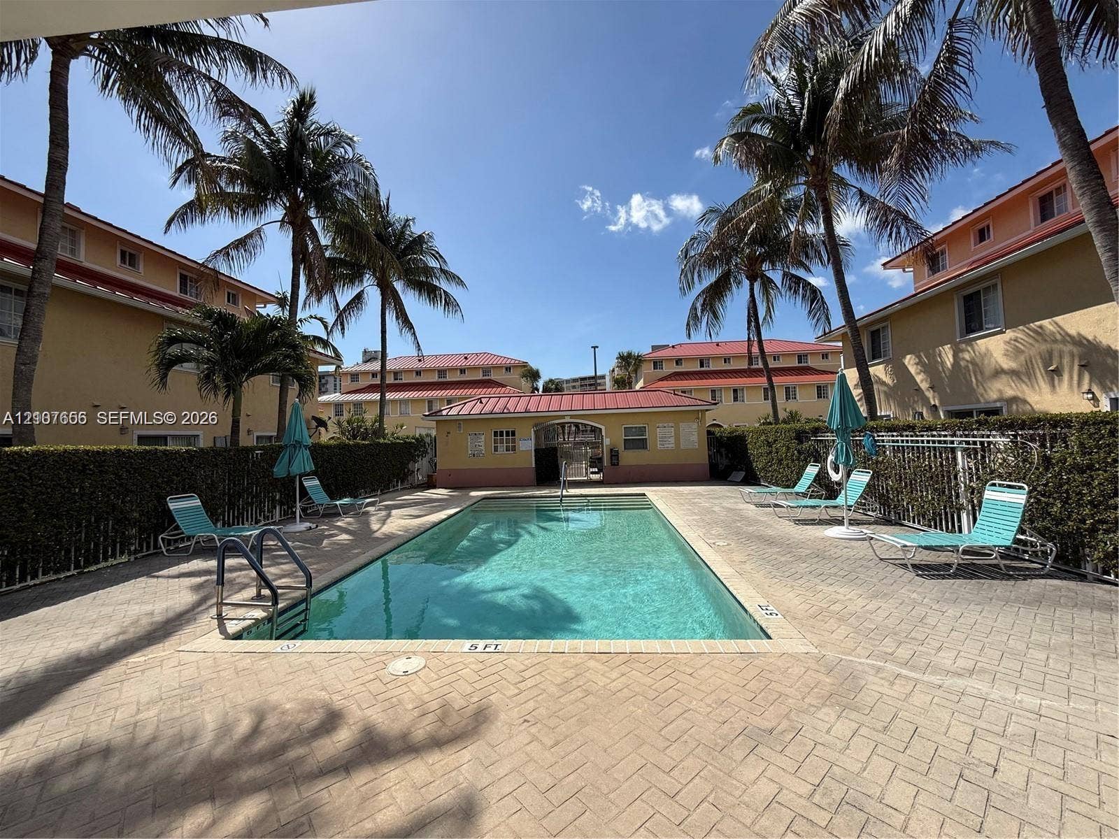 2088 NE 167th Street, #2-111, North Miami Beach, North Miami Beach, FL 33162 Outdoor swimming pool featuring a brick-paved deck, perimeter metal fencing, and mature palm trees
