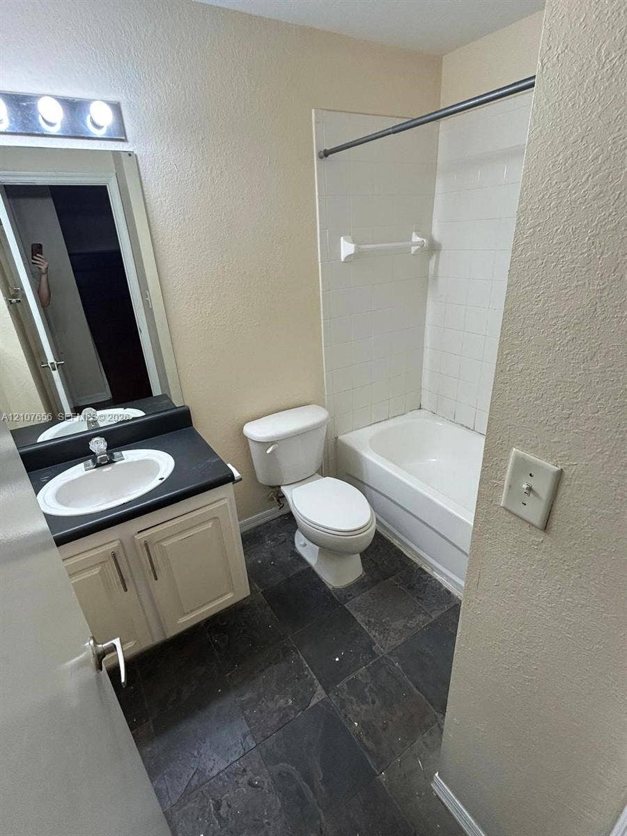 2088 NE 167th Street, #2-111, North Miami Beach, North Miami Beach, FL 33162 Bathroom featuring dark stone-style tile flooring, vanity with a dark countertop and integrated sink, full-width mirror, and a tub-shower combination with white wall tile