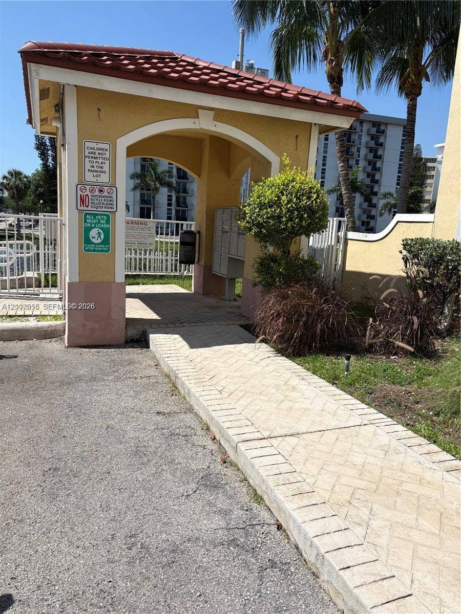 2088 NE 167th Street, #2-111, North Miami Beach, North Miami Beach, FL 33162 Covered entryway featuring a Spanish-tile roof, stucco columns with decorative arches, and an inlaid herringbone paver walkway