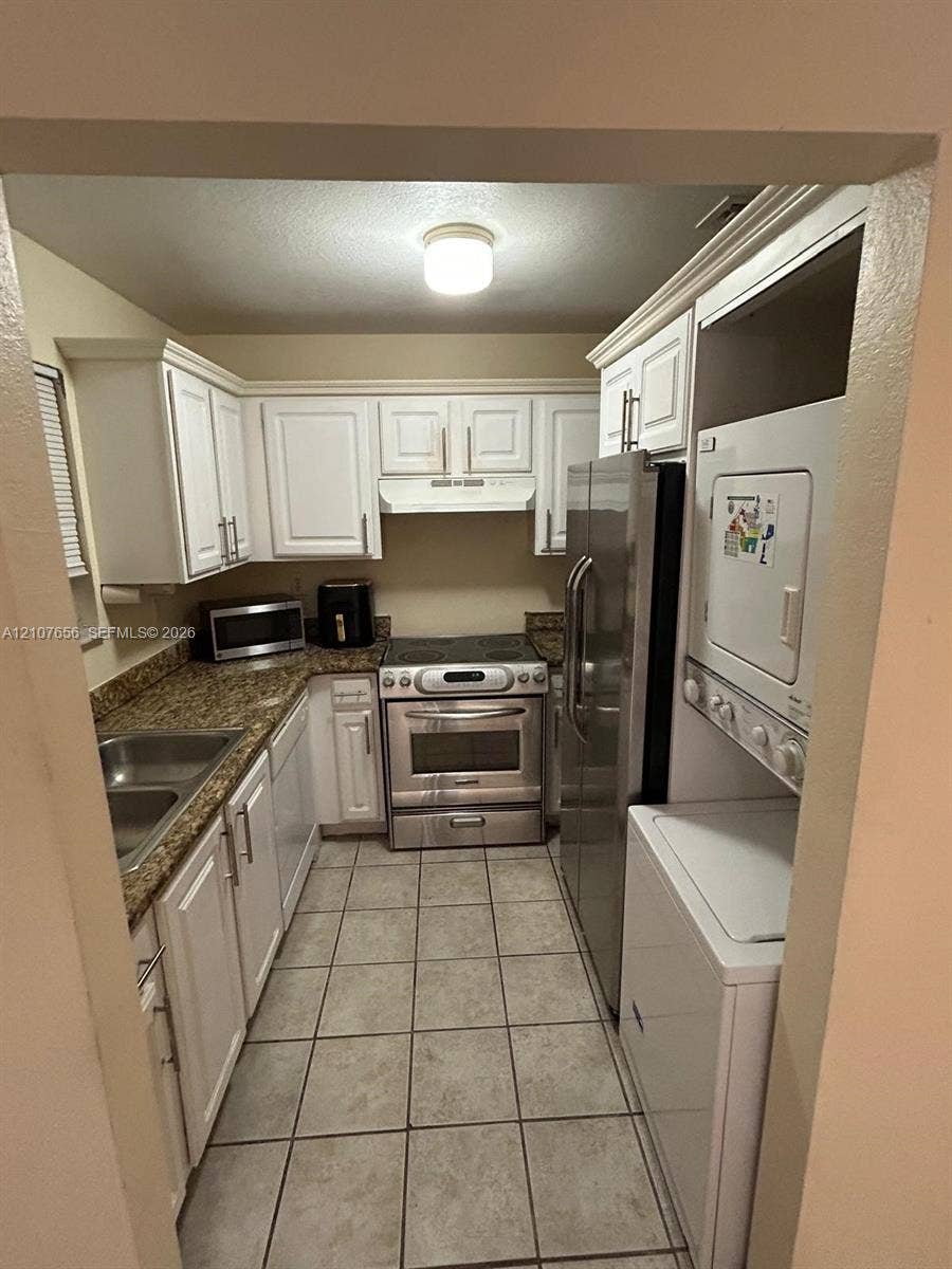 2088 NE 167th Street, #2-111, North Miami Beach, North Miami Beach, FL 33162 Kitchen featuring white shaker-style cabinetry, stone-finish countertops, stainless steel appliances, tile flooring, and integrated laundry appliances