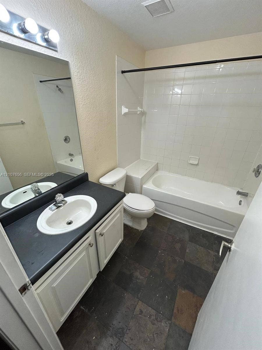 2088 NE 167th Street, #2-111, North Miami Beach, North Miami Beach, FL 33162 Bathroom featuring a vanity with dark countertop and inset oval sink, white cabinetry, tile flooring, and a tub-shower combination with full-height tile surround