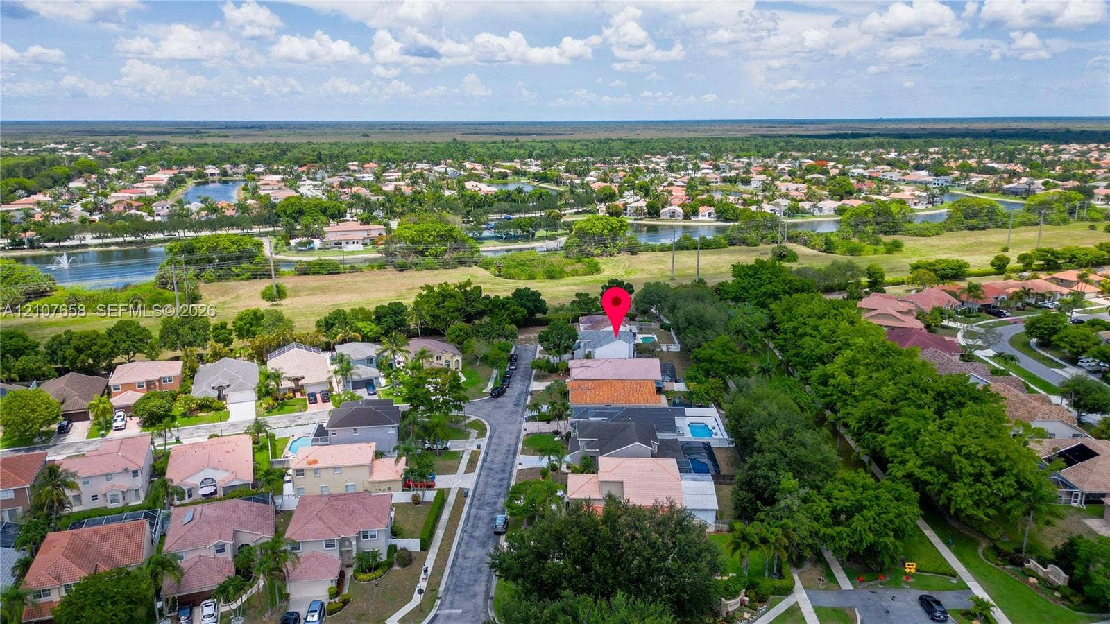 Aerial view of the residential property featuring a backyard swimming pool, paved driveway, multi-level roof structure, and surrounding landscape