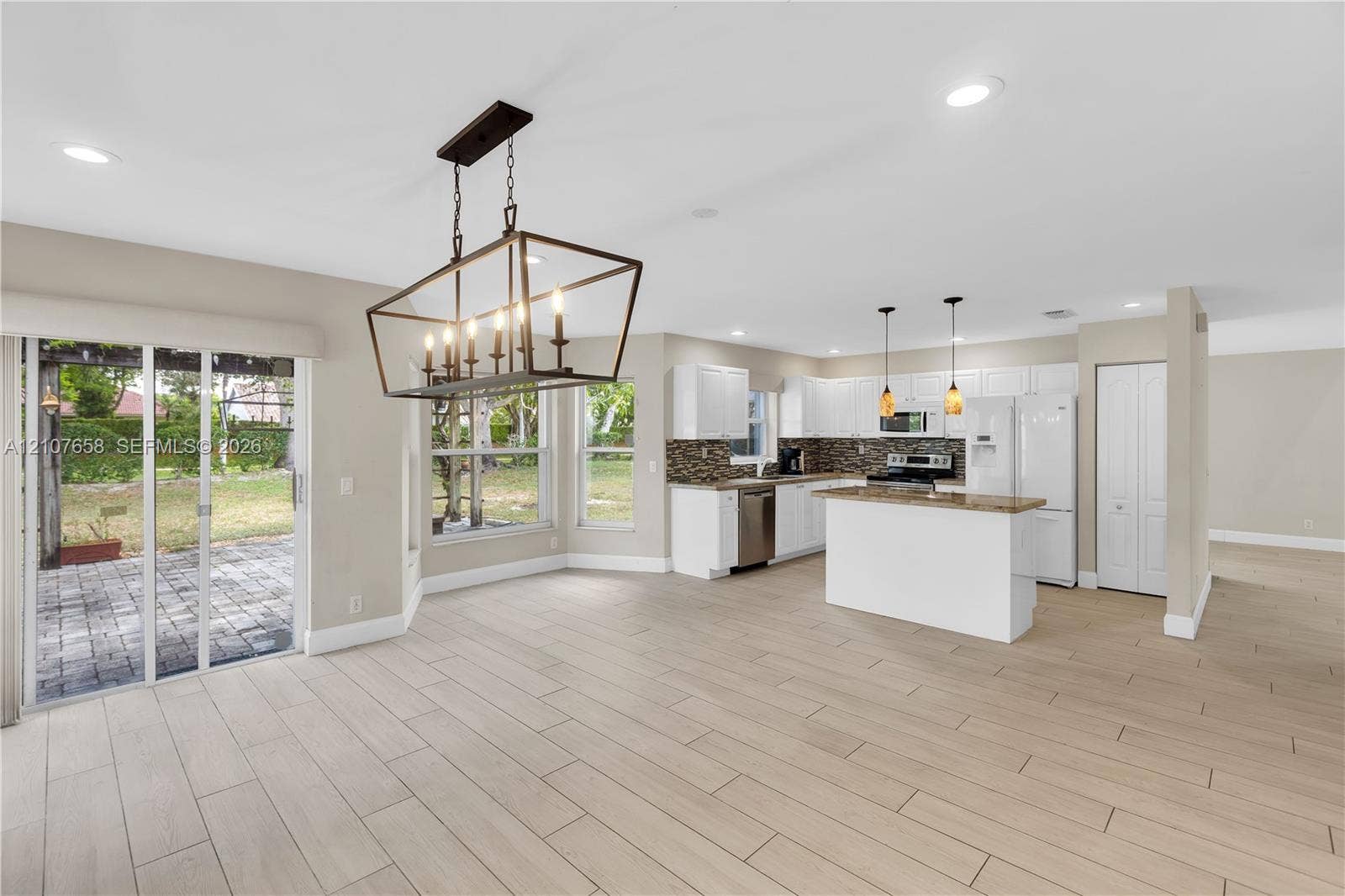Kitchen featuring a central island, white cabinetry, a tiled backsplash, wood-finish flooring, and a large metal-frame chandelier