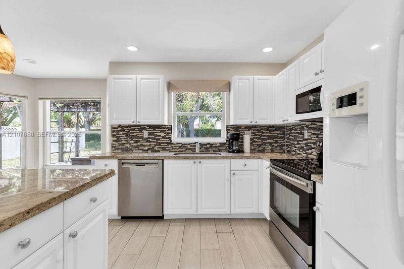 Kitchen featuring white cabinetry, stone countertops, stainless steel appliances, multi-tonal mosaic tile backsplash, and wood-finish flooring