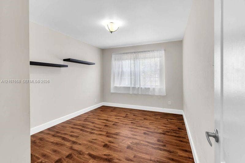 Interior room featuring wood-finish flooring, neutral wall tones, dual built-in wall shelves, and a flush-mount ceiling light fixture