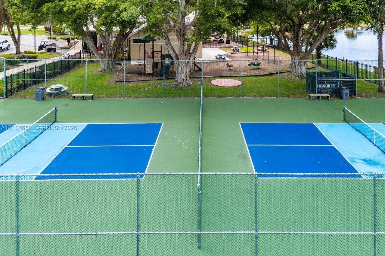 Dual pickleball courts featuring perimeter chain-link fencing, mature shade trees, and a ground-level recreational area