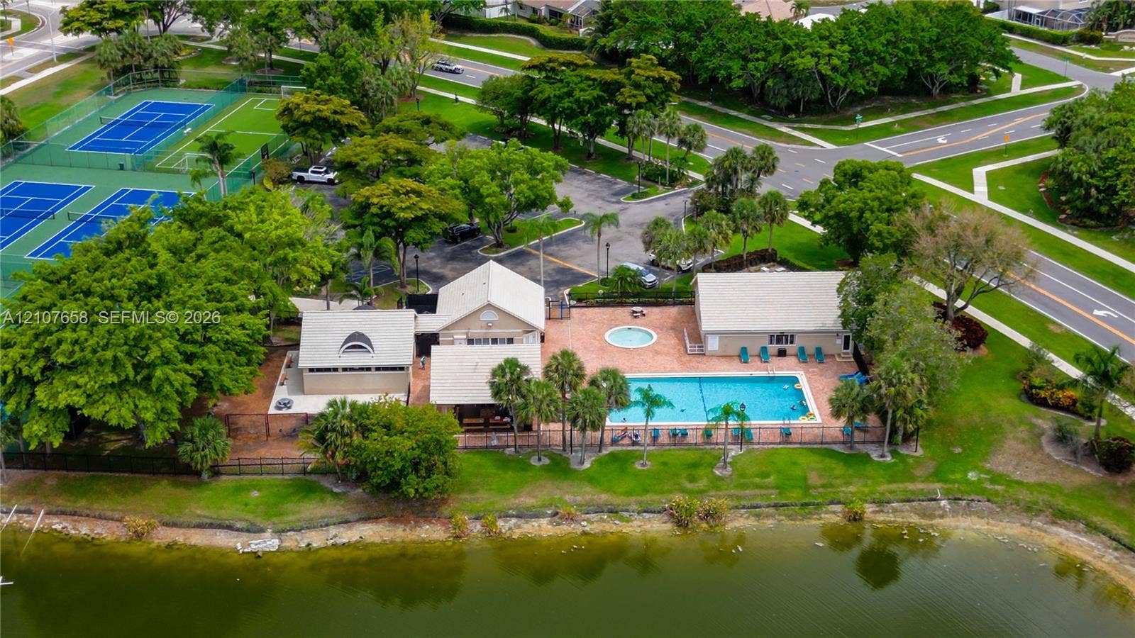 Recreational facility featuring a swimming pool, spa, and tennis courts situated along a waterfront