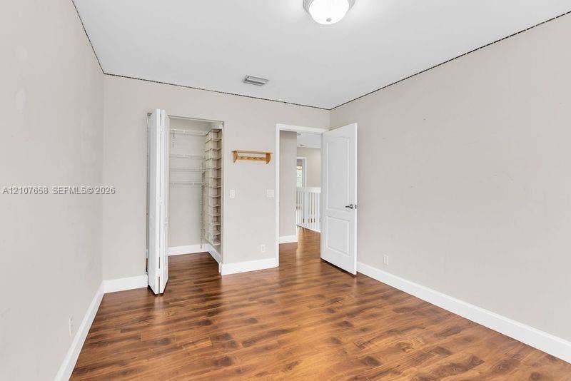 Room featuring wood-finish flooring, neutral wall paint, and a built-in closet with shelving