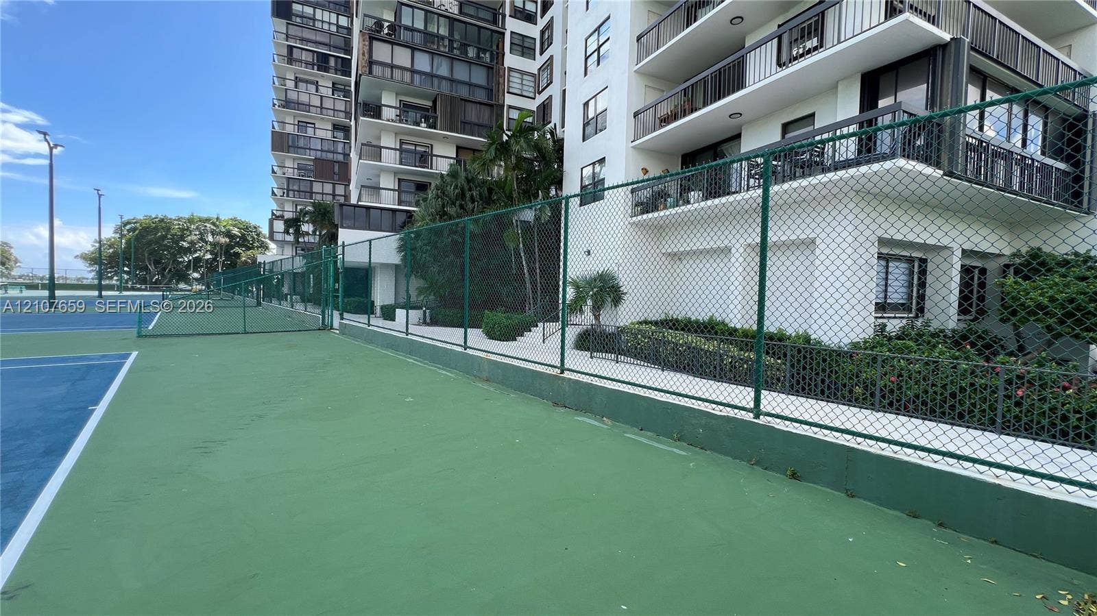 Hard-surfaced tennis court with perimeter chain-link fencing and high-mast exterior lighting