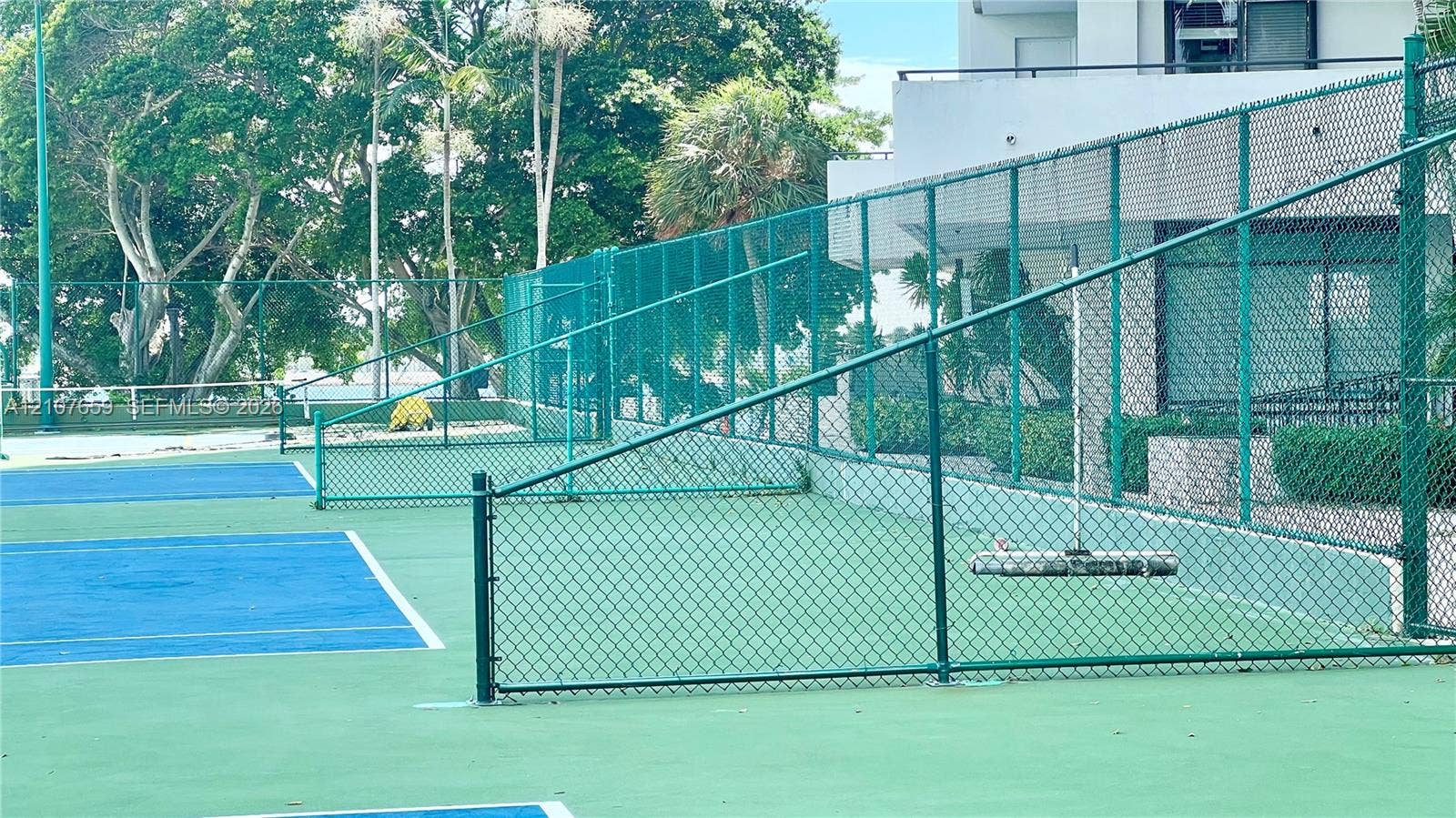Tennis court with hard-surface playing area, perimeter chain-link fencing, and overhead court lighting