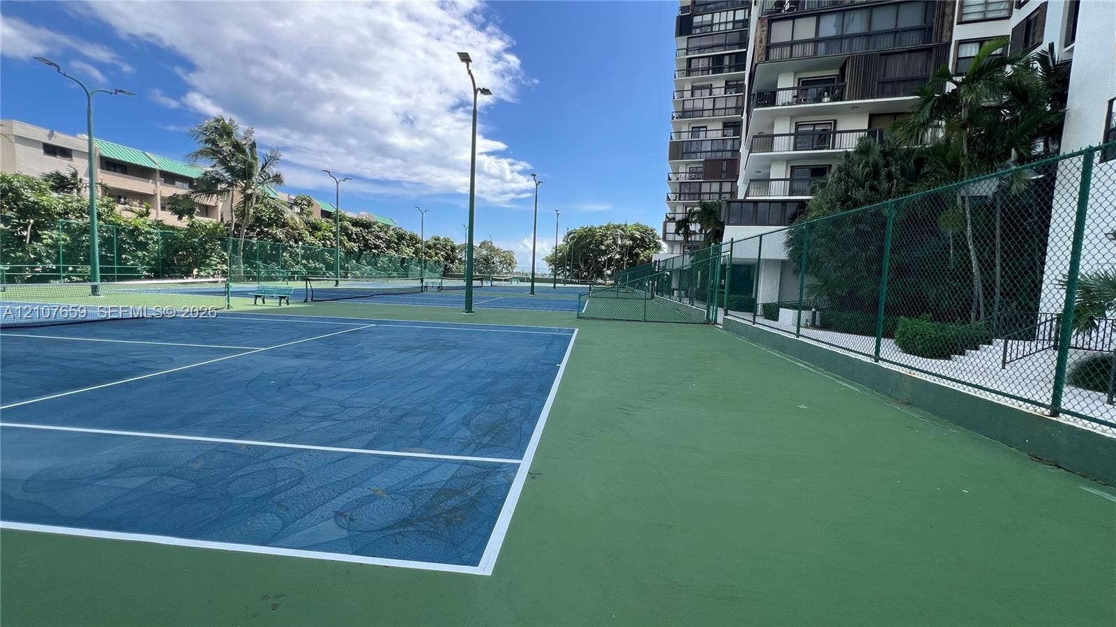 Multi-court tennis facility featuring blue and green surface color blocking, perimeter chain-link fencing, and overhead court lighting