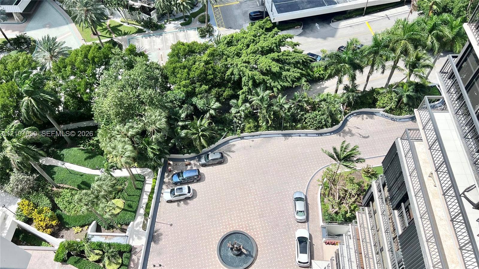 Elevated perspective of the property grounds featuring a paved circular motor court, decorative central fountain, manicured perimeter landscaping, and mature palm trees