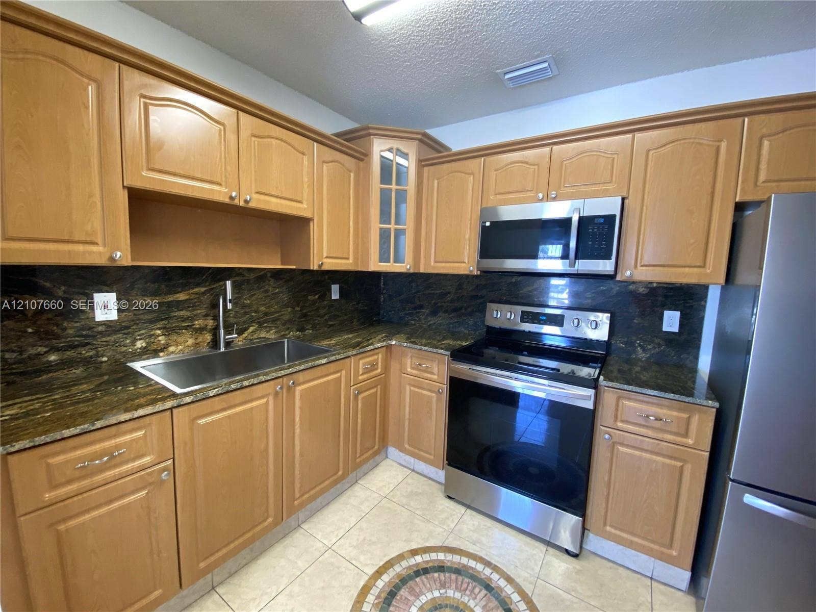 Kitchen featuring light wood-finish cabinetry, stone countertops, stainless steel appliances, a single-basin undermount sink, and tiled flooring