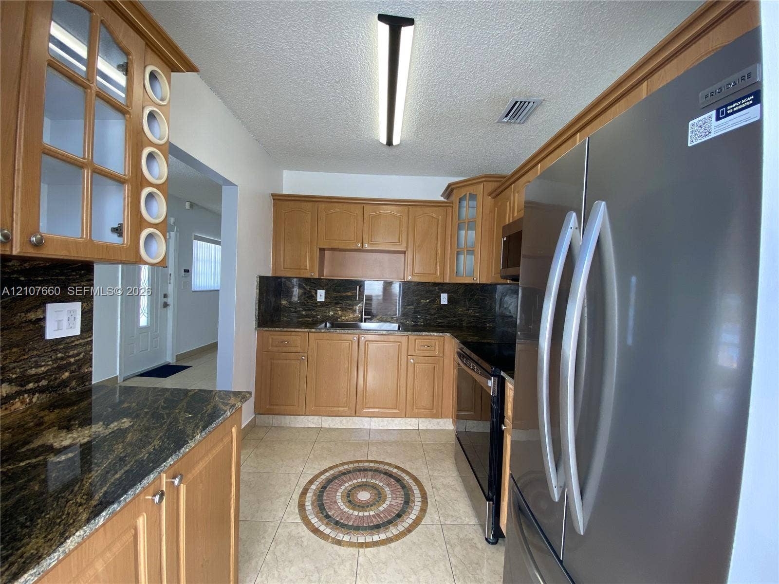 Kitchen featuring natural wood cabinetry, stone countertops, stainless steel refrigerator, electric range, and tiled flooring with a decorative mosaic inlay