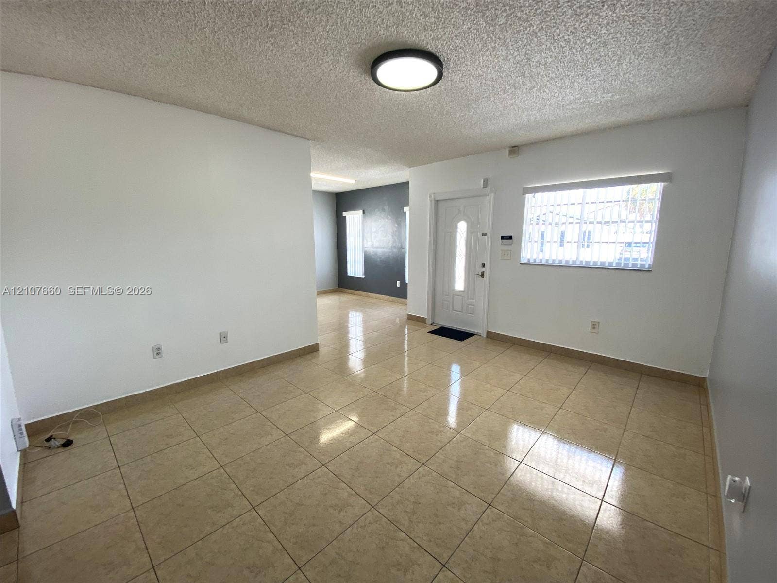 Interior space featuring neutral-toned tile flooring, recessed flush-mount ceiling lighting, textured ceiling finish, and an exterior door with decorative glass paneling