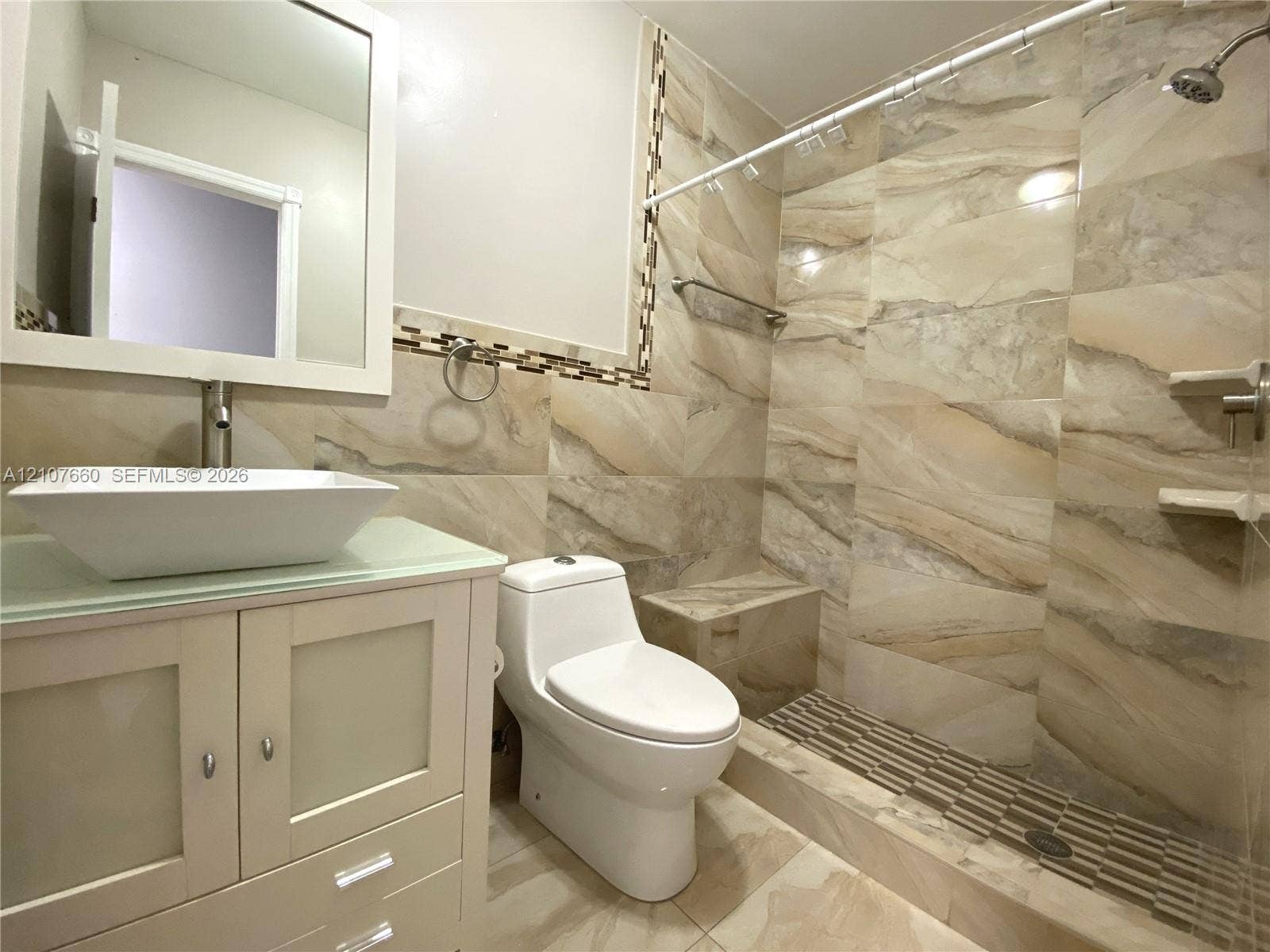 Bathroom featuring a vessel sink with a glass-topped vanity, large-format tile wall cladding, a walk-in shower with a built-in bench, and mosaic tile accents