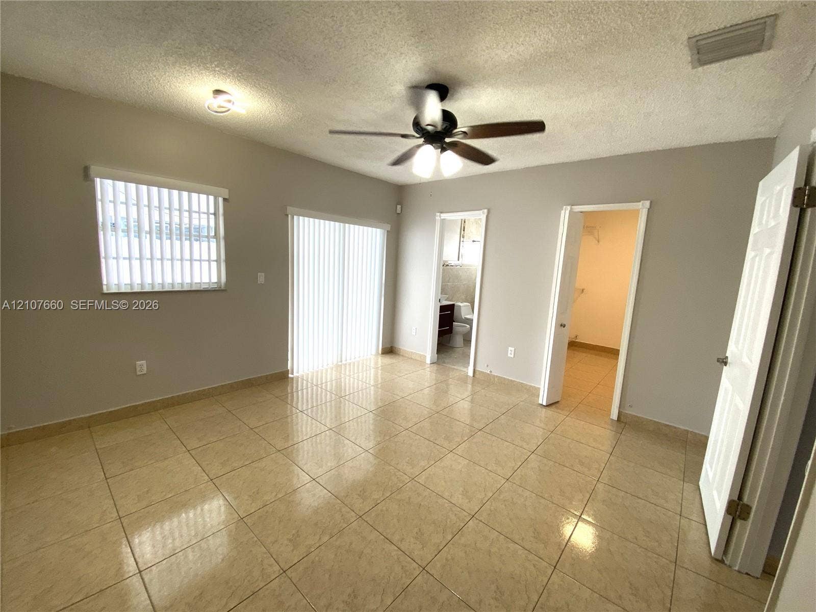Neutral-toned room featuring tiled flooring, a ceiling fan with integrated lighting, a sliding glass door, and a single-hung window with vertical blinds