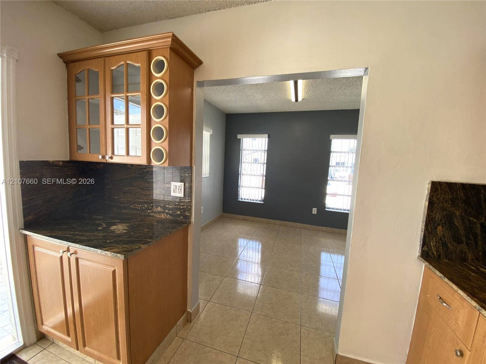 Custom cabinetry featuring glass-panel upper doors and built-in circular wine storage, stone countertops, and polished tile flooring