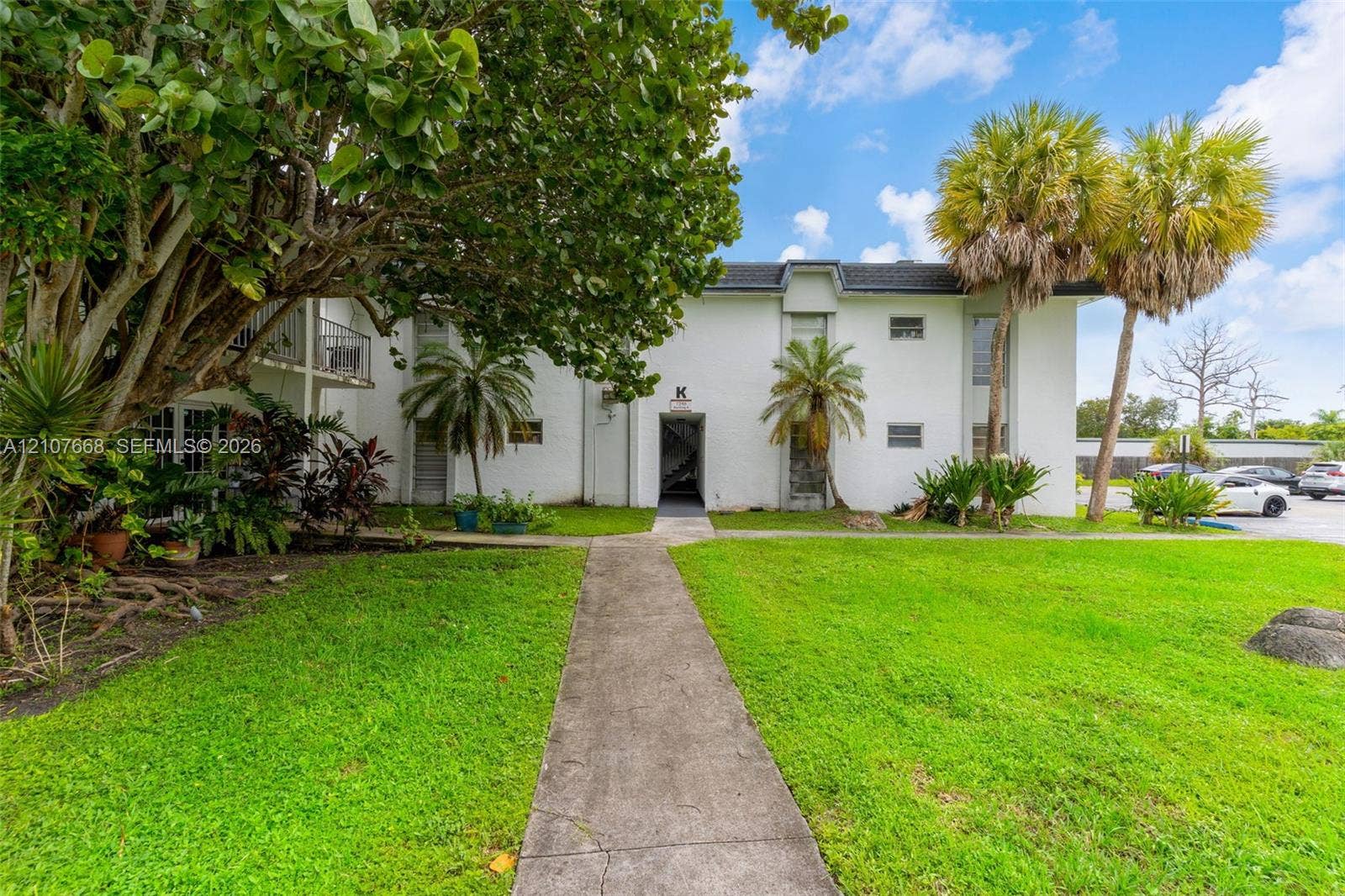 7245 SW 94th Place, #K4, Miami, FL 33173 Multi-story exterior featuring white stucco siding, a concrete pathway, mature trees, and palm landscaping