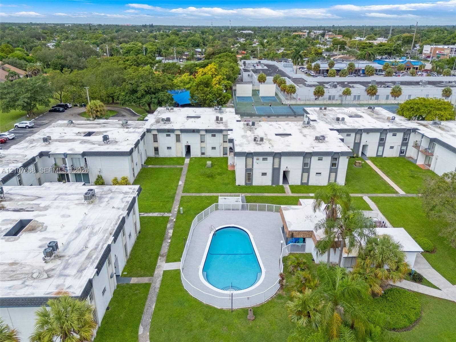 7245 SW 94th Place, #K4, Miami, FL 33173 Aerial perspective of the multi-unit complex featuring an outdoor swimming pool with surround decking, mature palms, manicured lawns, and paved walkways