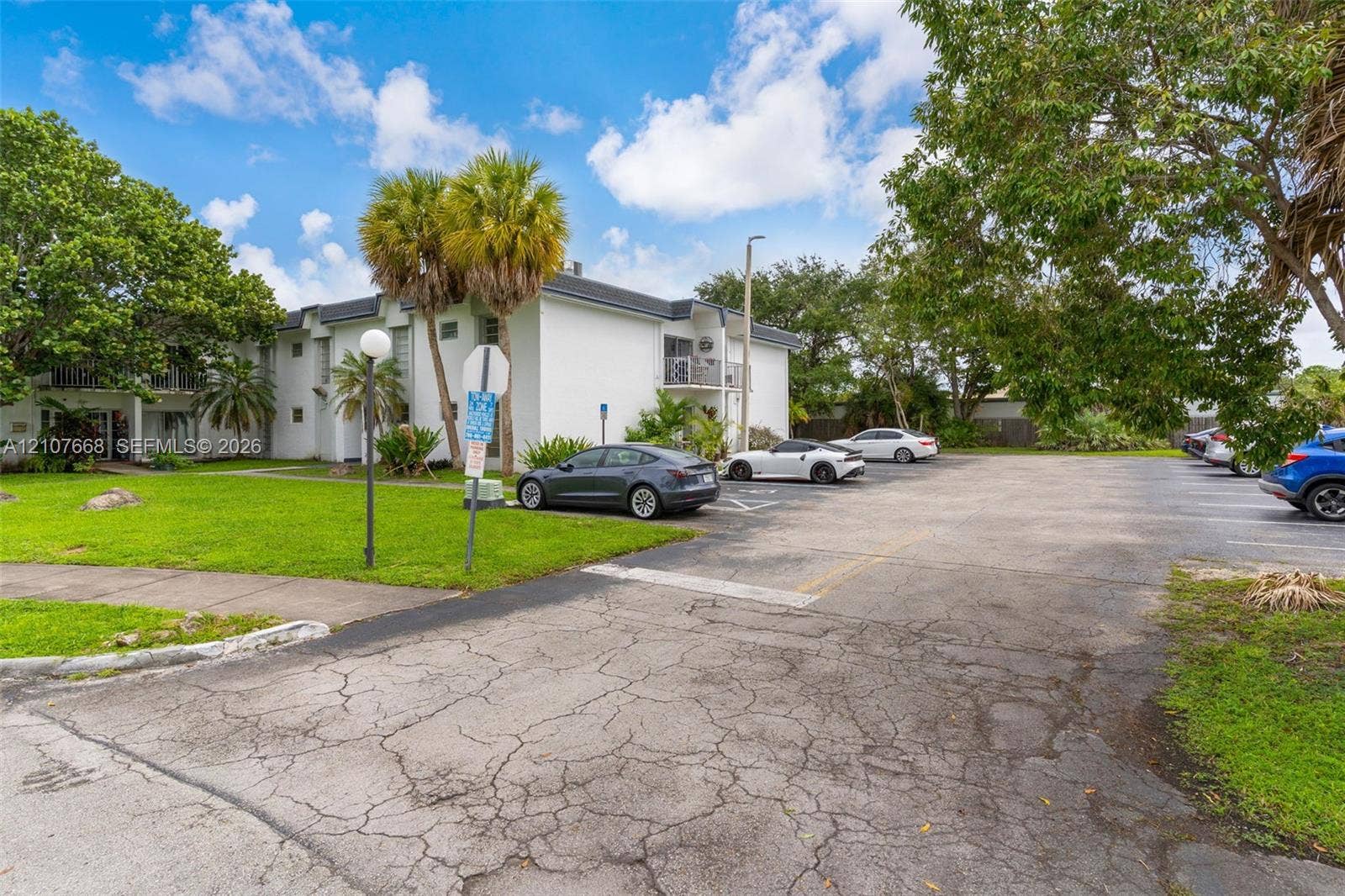 7245 SW 94th Place, #K4, Miami, FL 33173 Multi-story building exterior featuring smooth white siding, paved surface parking, and mature palm and shade trees