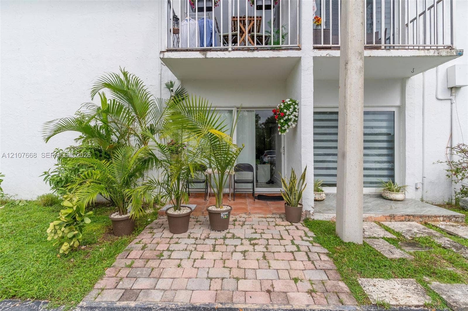 7245 SW 94th Place, #K4, Miami, FL 33173 Ground-level patio featuring interlocking concrete pavers, sliding glass entry doors, and a second-story balcony with metal railing