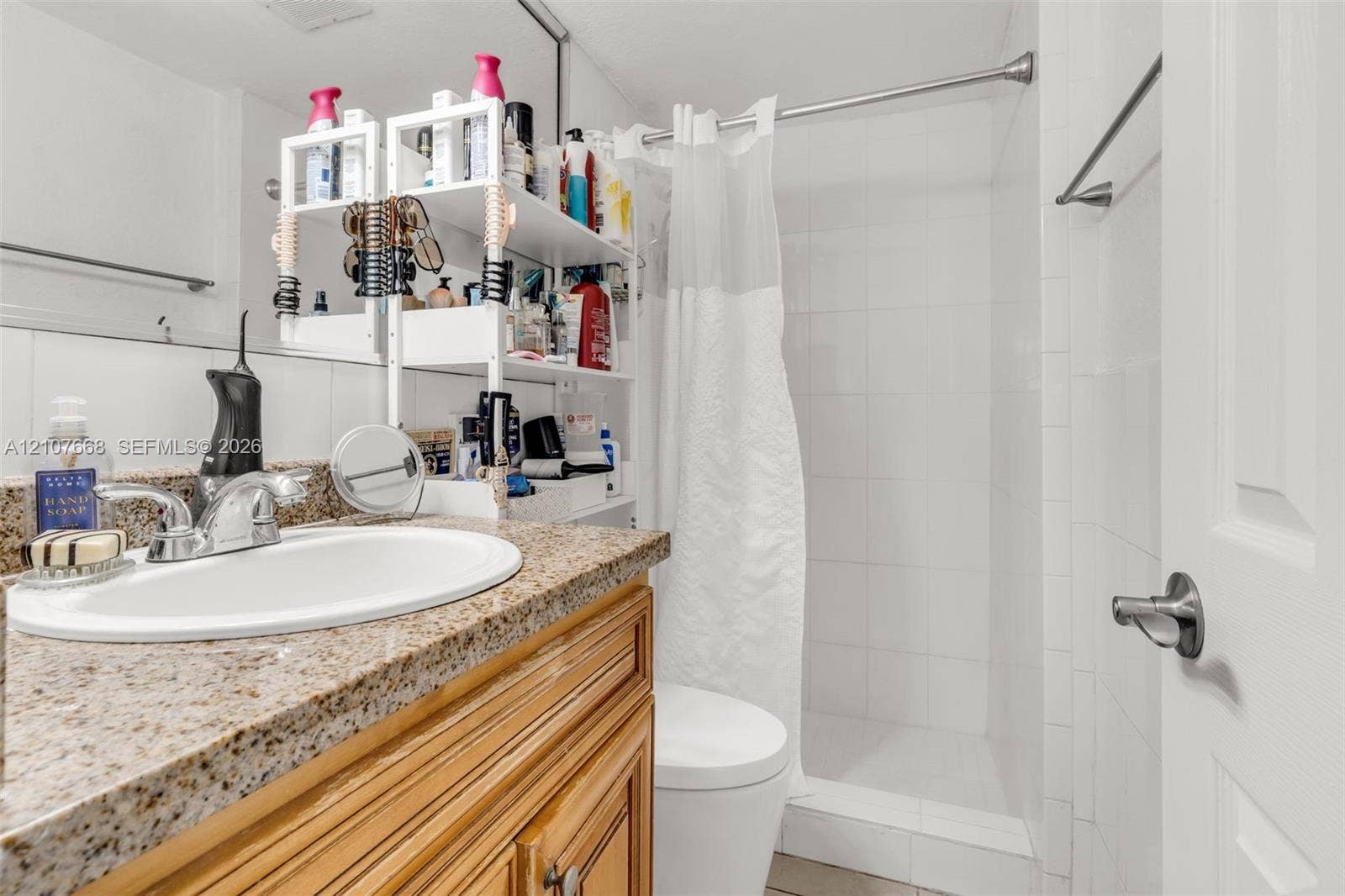 7245 SW 94th Place, #K4, Miami, FL 33173 Bathroom featuring a natural stone-finish countertop, undermount sink with chrome-finish faucet, wood cabinetry, and a walk-in shower with white tile surround