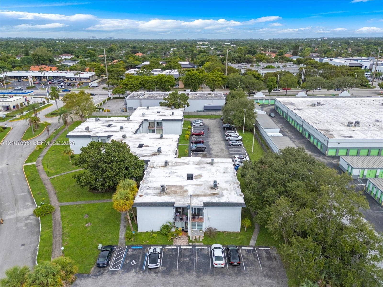 7245 SW 94th Place, #K4, Miami, FL 33173 Multi-level building exterior featuring a flat roofline, painted masonry facade, assigned asphalt parking, and landscaped grounds with mature trees