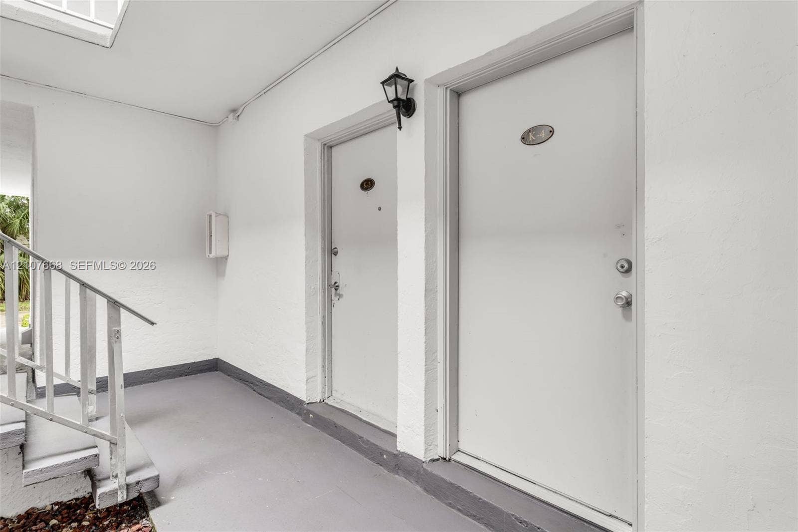 7245 SW 94th Place, #K4, Miami, FL 33173 Covered entryway featuring white exterior walls, painted concrete flooring, a metal staircase with railing, and wall-mounted exterior lighting
