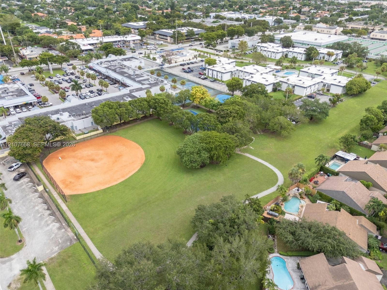 7245 SW 94th Place, #K4, Miami, FL 33173 Aerial view of a sprawling recreational area featuring an expansive grass field, a dedicated baseball diamond, paved walkways, and mature trees