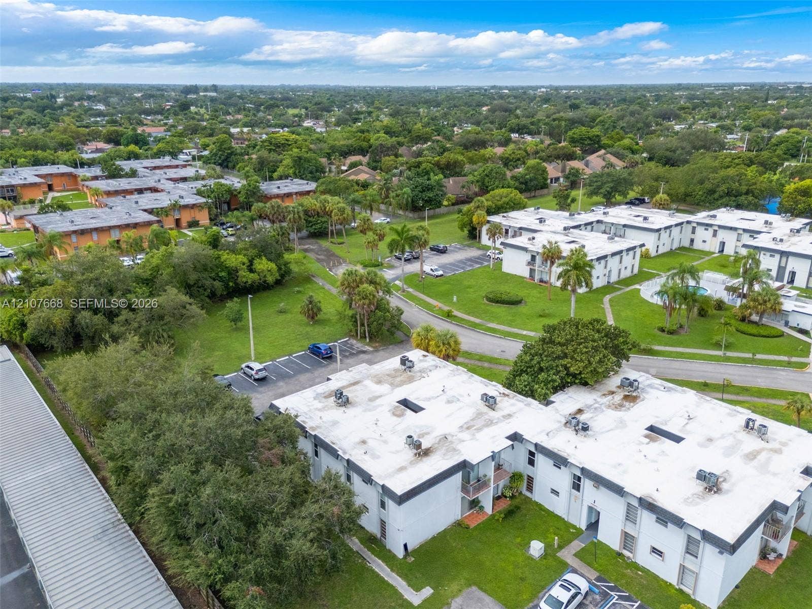 7245 SW 94th Place, #K4, Miami, FL 33173 Aerial perspective featuring multi-unit structures, landscaped grounds with mature palm trees, dedicated surface parking, and a communal swimming pool