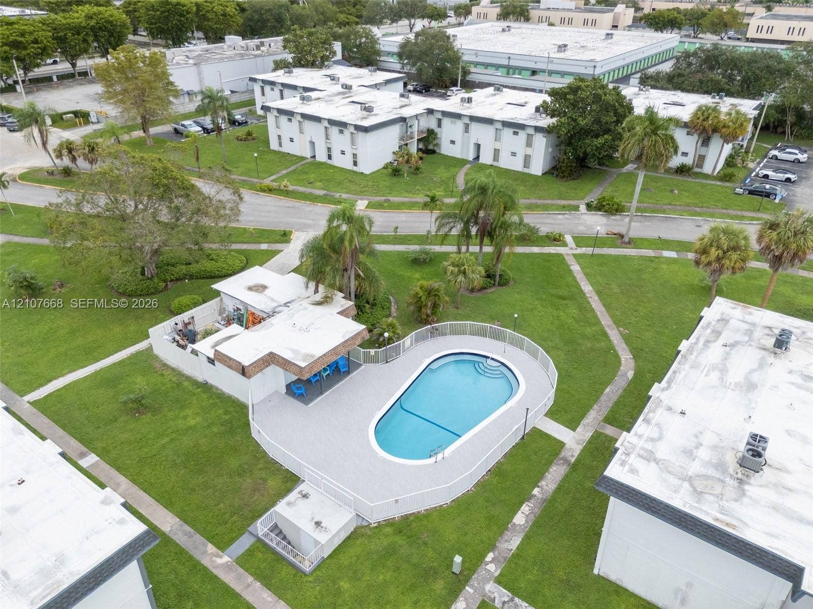 7245 SW 94th Place, #K4, Miami, FL 33173 Swimming pool with surrounding paver deck, white perimeter fencing, and covered cabana area situated within expansive landscaped grounds