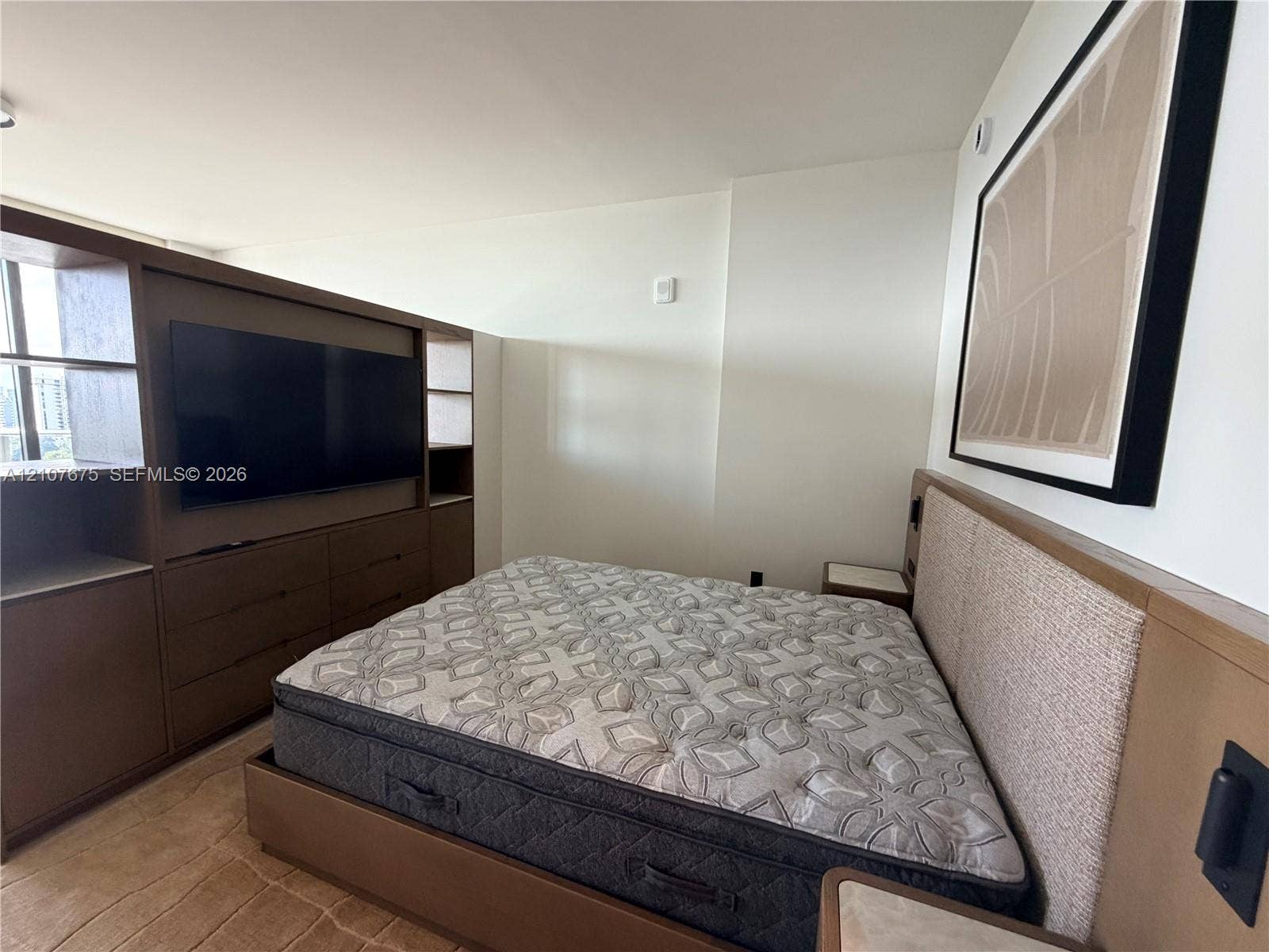 Built-in wood-finish cabinetry with integrated shelving and flat-panel storage, custom wood-finish platform frame with textile-upholstered headboard, and integrated surface-mounted bedside nightstands