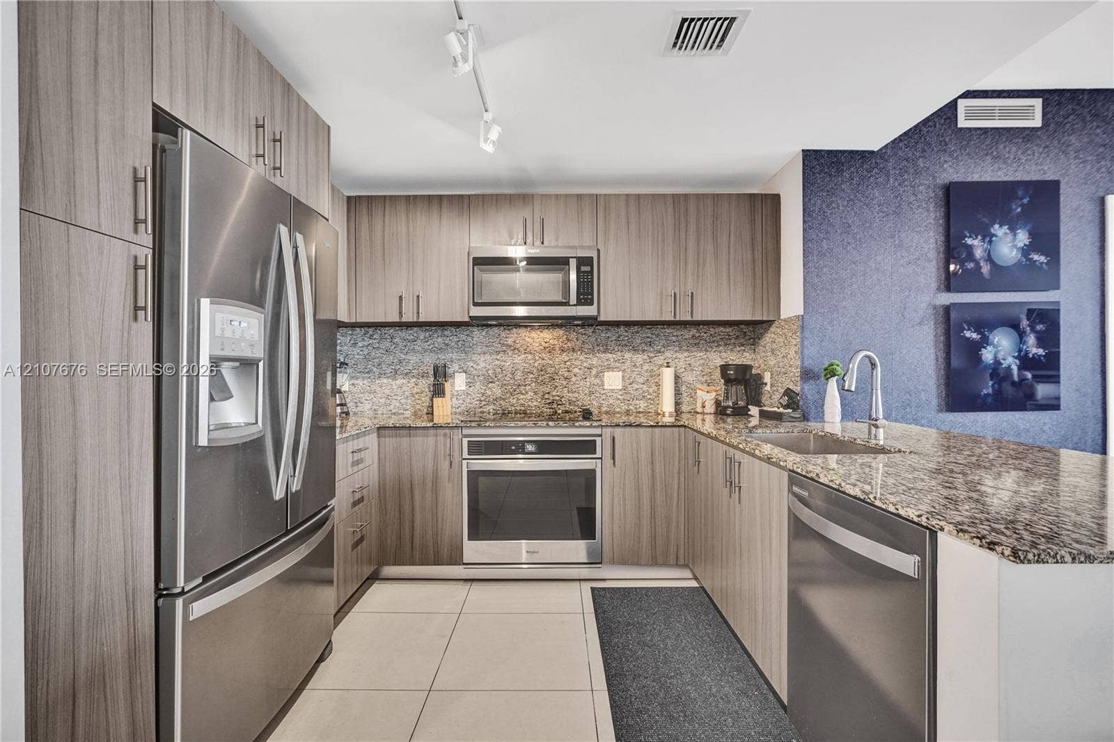 5350 NW 84th Avenue, #1004, Doral, FL 33166 Kitchen featuring wood-finish cabinetry, stainless steel appliances, stone-surface countertops, tile flooring, and track lighting