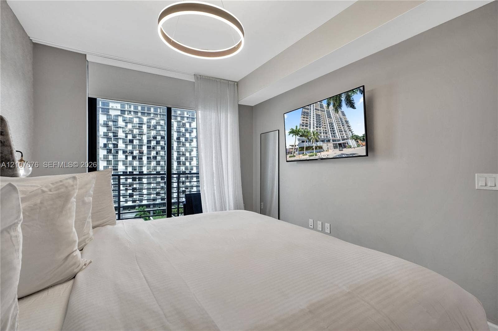 5350 NW 84th Avenue, #1004, Doral, FL 33166 Floor-to-ceiling glass sliding doors opening to a private balcony, contemporary circular LED chandelier, and wall-mounted television