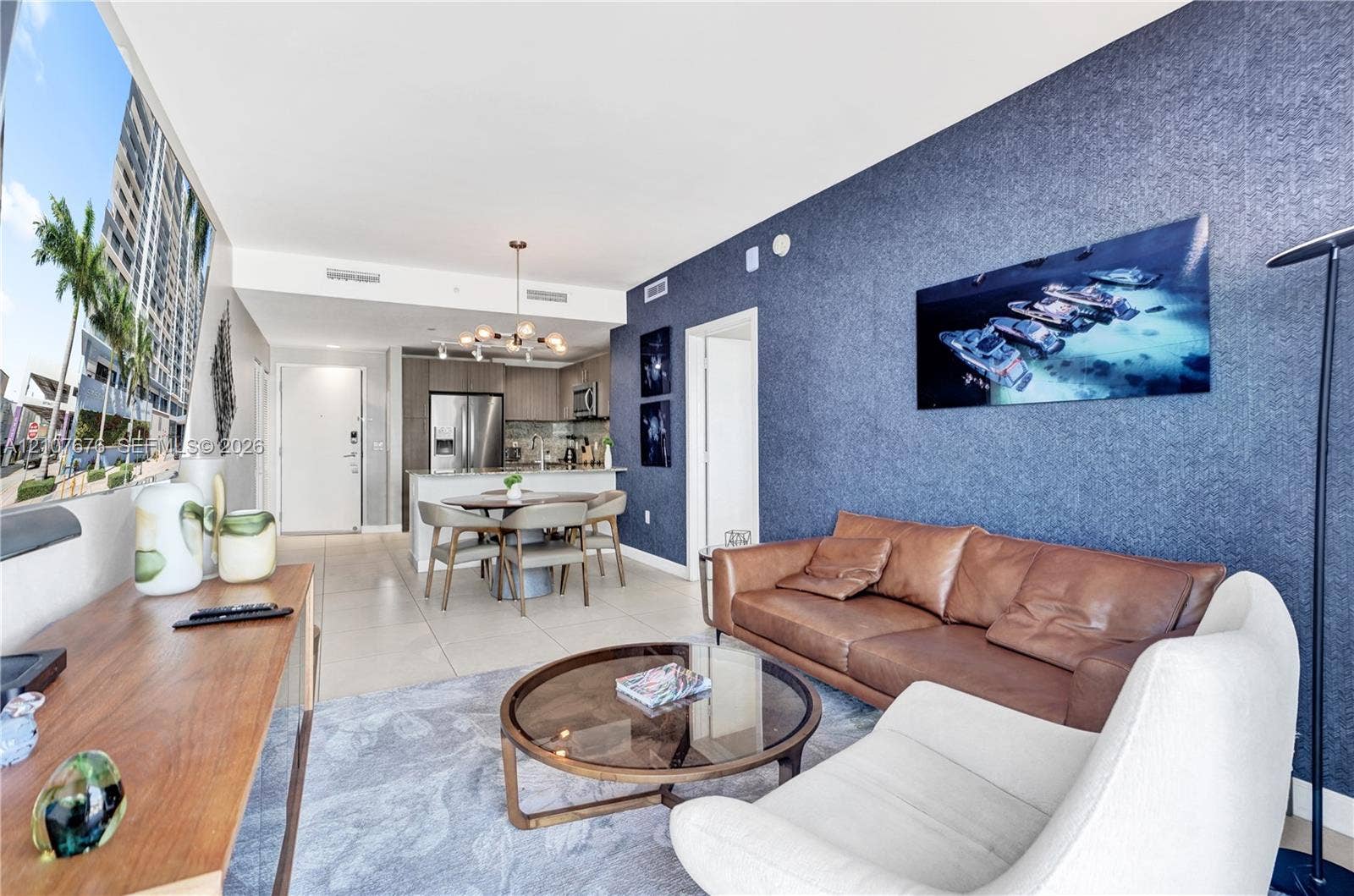 5350 NW 84th Avenue, #1004, Doral, FL 33166 Open-concept living space featuring large-format tile flooring, a prominent textured navy accent wall, stainless steel kitchen appliances, and a contemporary multi-light chandelier