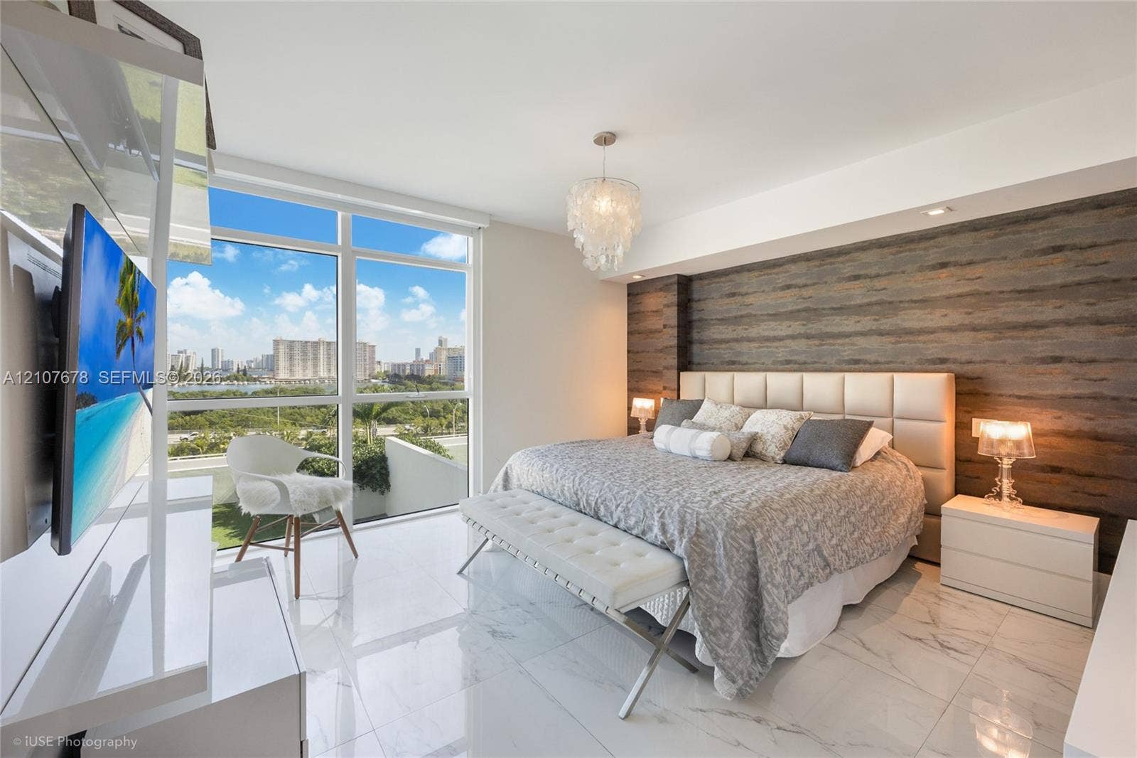 400 Sunny Isles Boulevard, #704, Sunny Isles Beach, FL 33160 Floor-to-ceiling windows, wood-panel accent wall, polished stone-finish flooring, and decorative chandelier