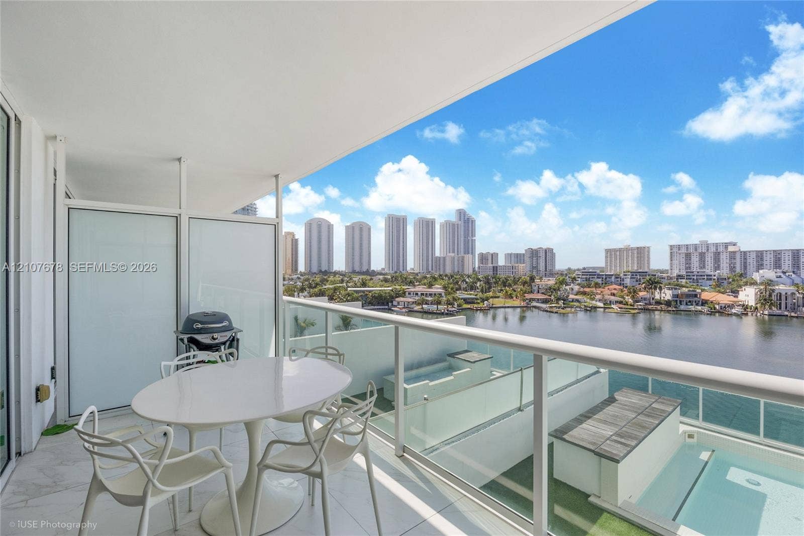 400 Sunny Isles Boulevard, #704, Sunny Isles Beach, FL 33160 Covered balcony featuring stone-finish flooring, glass panel railing, and frosted privacy partitions, overlooking a waterfront skyline