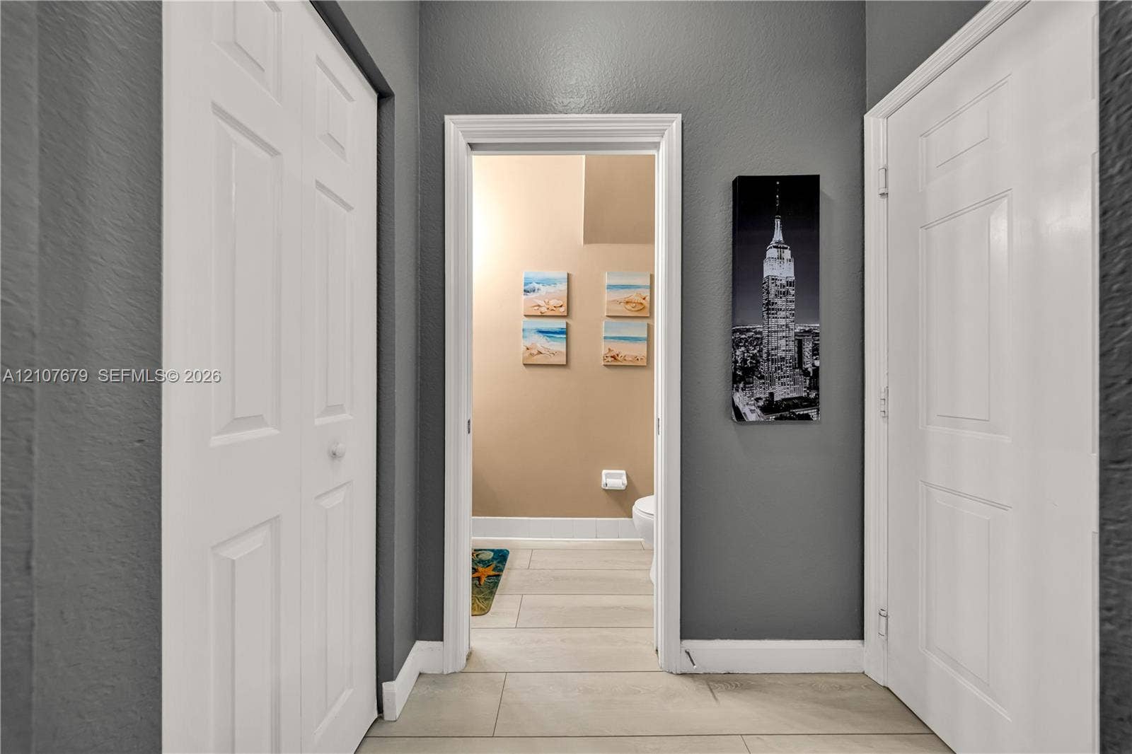 22066 SW 93rd Place, Cutler Bay, FL 33190 Interior hallway featuring neutral grey wall paint, two white six-panel closet doors, a white interior door, and ceramic tile flooring