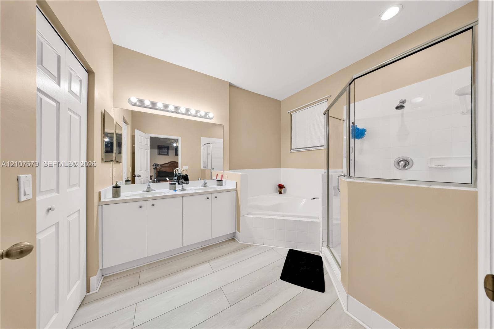 22066 SW 93rd Place, Cutler Bay, FL 33190 Dual-sink vanity with white cabinetry, rectangular drop-in sinks, wall-to-wall mirror, tiled soaking tub, and enclosed glass shower with white surround