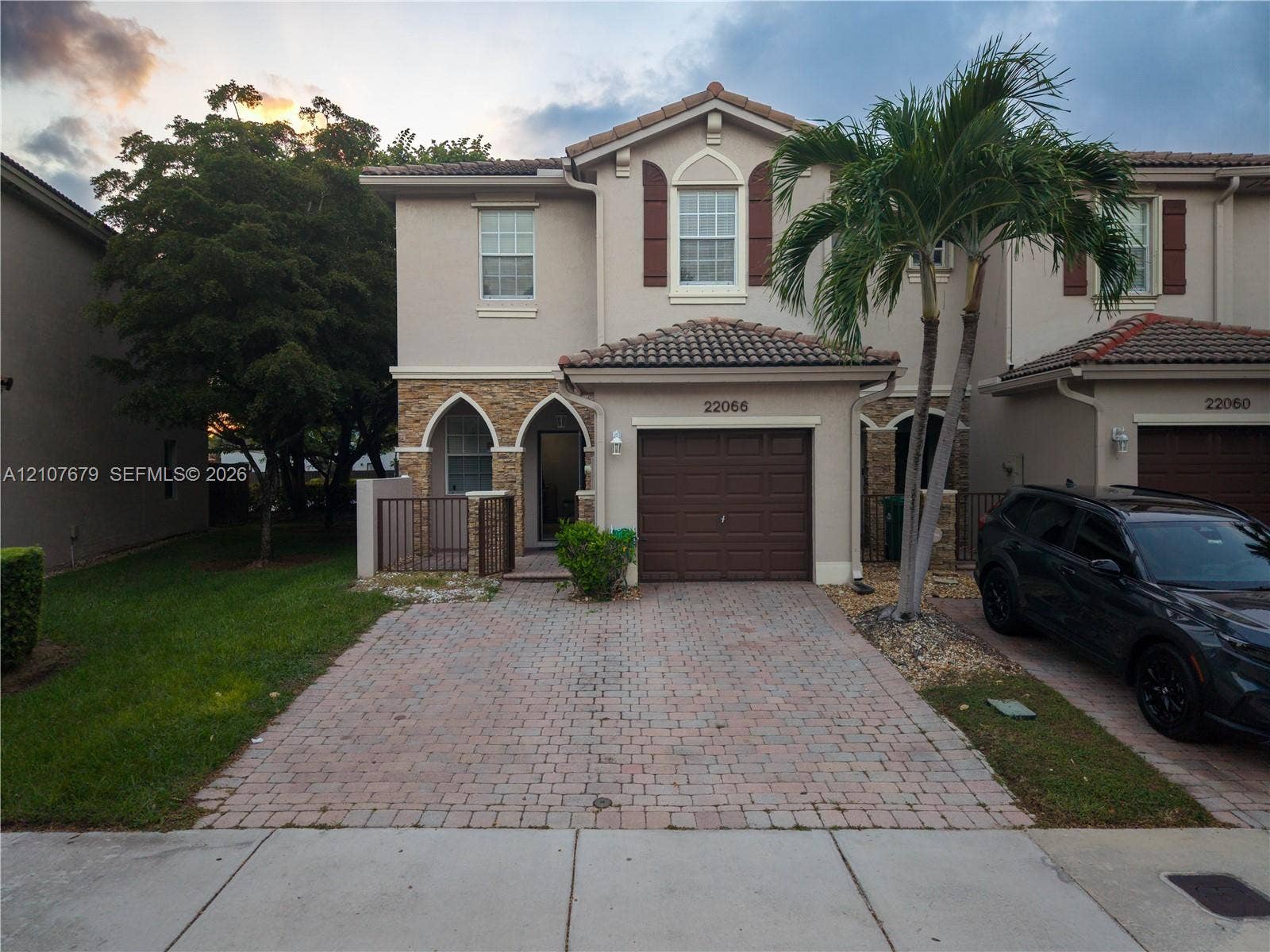 22066 SW 93rd Place, Cutler Bay, FL 33190 Two-story residence featuring a tile roof, stucco exterior with stone veneer accents, arched entryway, brick-paver driveway, and an attached single-car garage